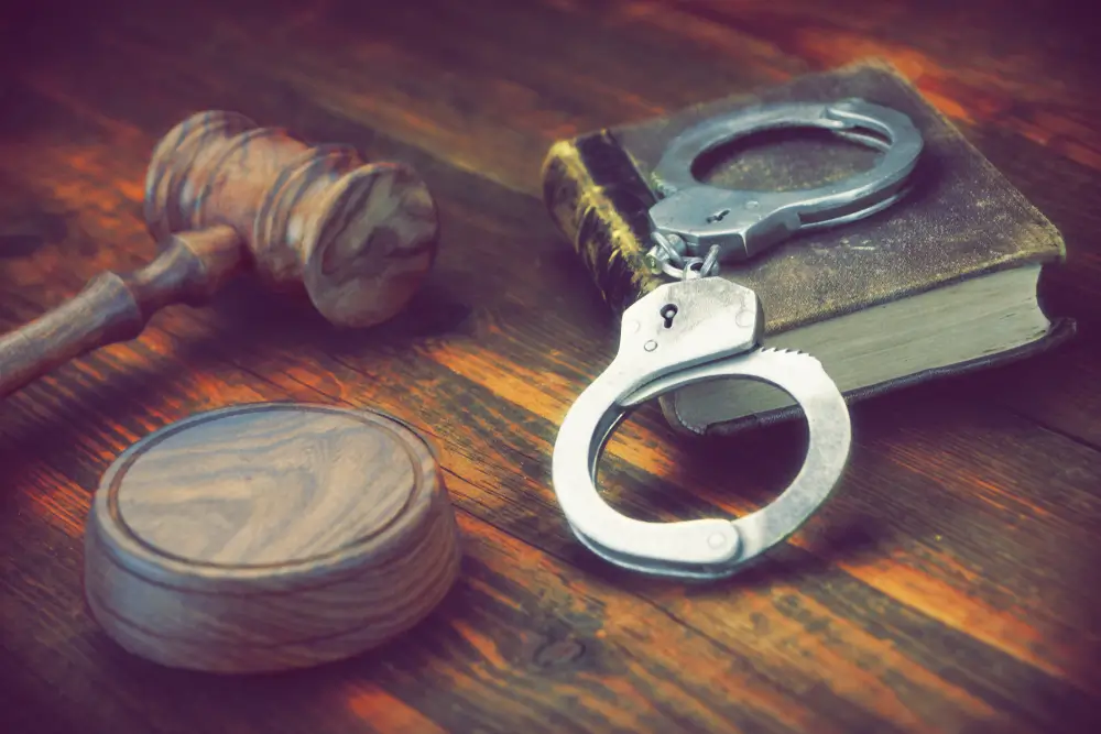Manette poggiate su un codice penale accanto a un martelletto in legno, simboli dell'attività di polizia giudiziaria.