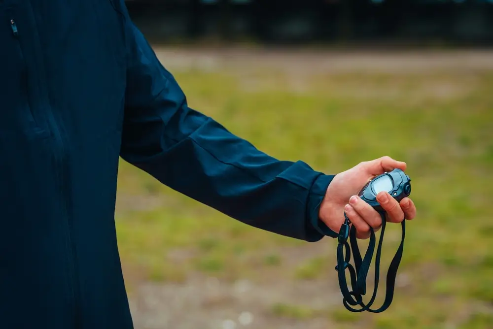 Allenatore cronometra una corsa di atletica con un cronometro digitale durante una prova di selezione.