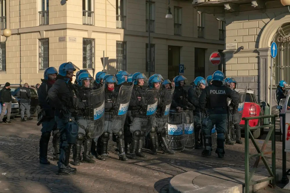 Agenti della Polizia di Stato in formazione con scudi e caschi antisommossa schierati in una via cittadina.