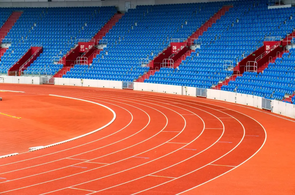 Pista di atletica rossa con corsie bianche e tribune blu, sede per gli accertamenti di efficienza fisica del concorso.
