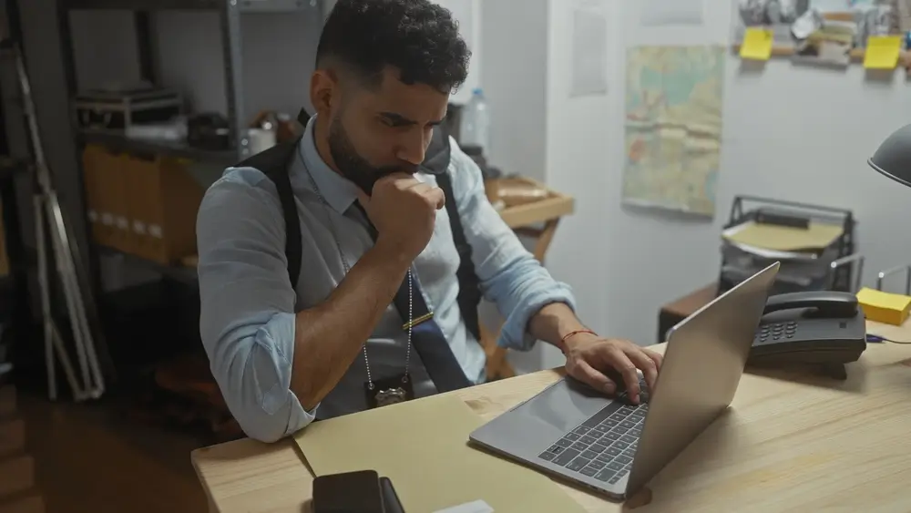 Ispettore al lavoro in un ufficio del commissariato di polizia, concentrato al laptop con distintivo e fondina.