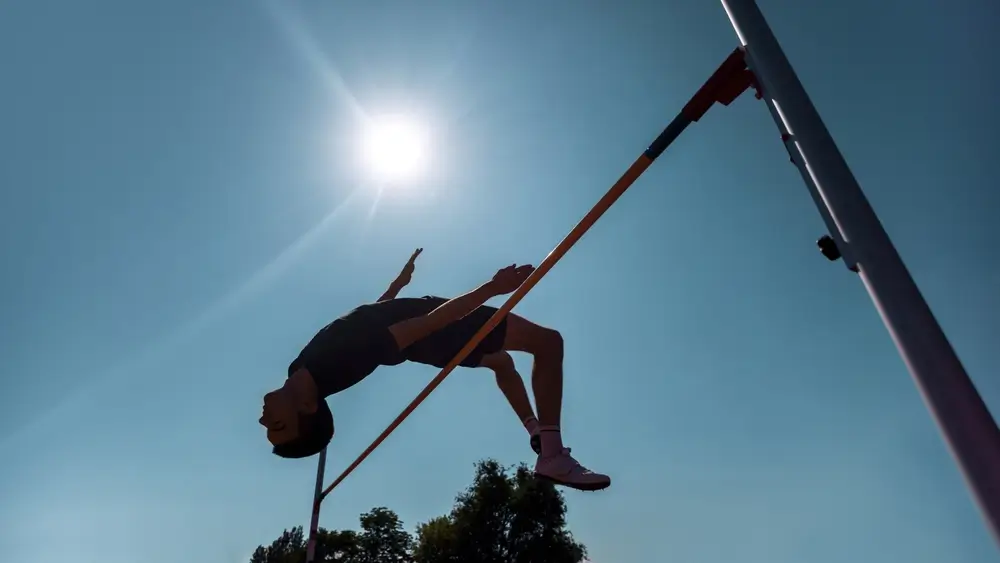Atleta di salto in alto che supera l'asticella con la tecnica Fosbury durante una prova di idoneità sotto il sole.