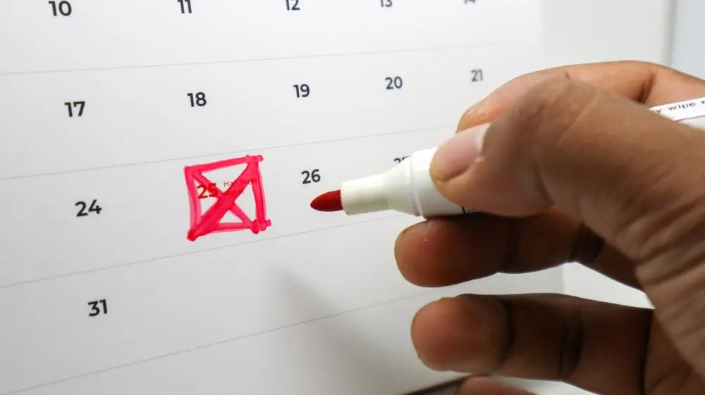 Mano che segna una data su un calendario con un pennarello rosso per la pianificazione delle scadenze del concorso.