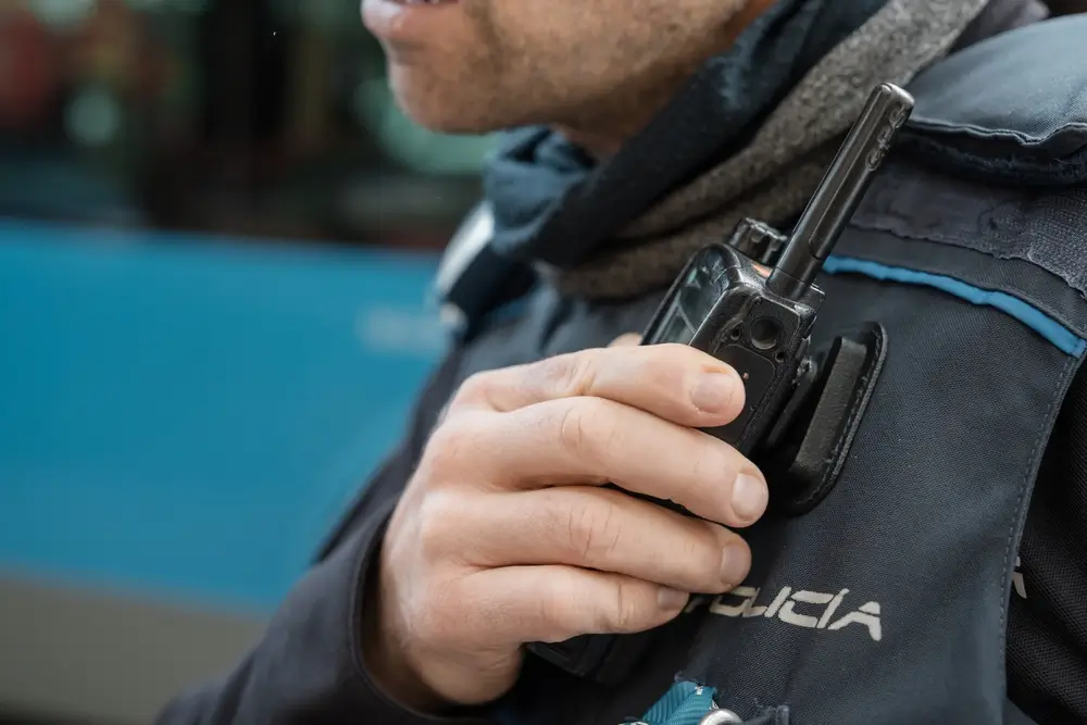 Agente di polizia in servizio che utilizza l'apparecchio radio ricetrasmittente fissato alla divisa tattica.
