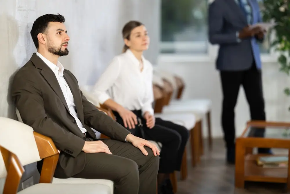 Candidati in abito formale seduti in una sala d'attesa per le prove e gli accertamenti del concorso in Polizia.