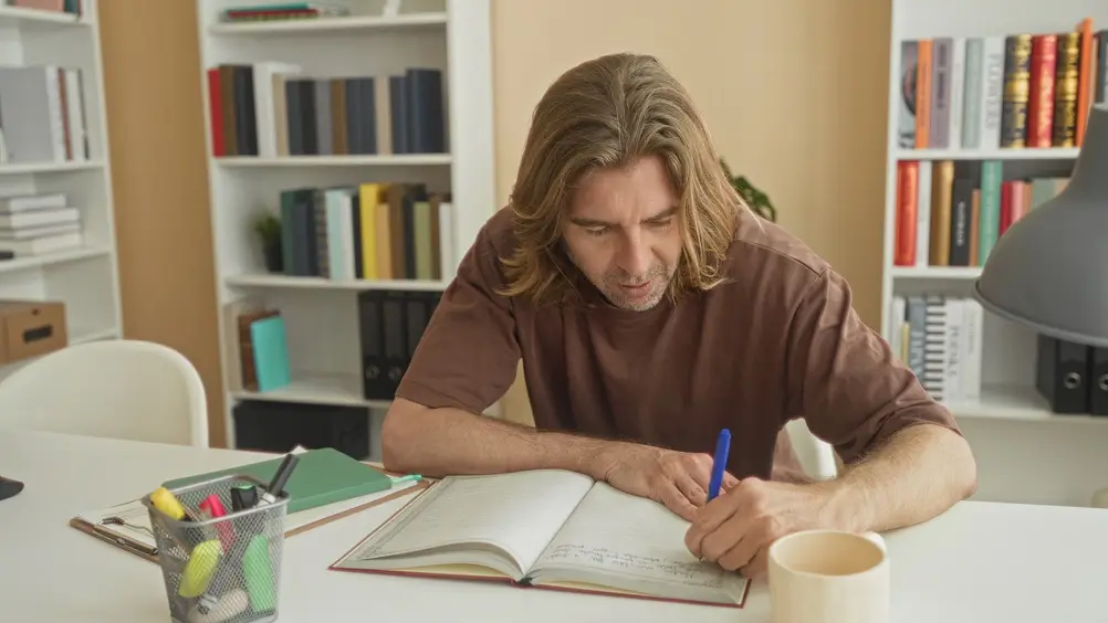 Uomo concentrato che prende appunti su un libro alla scrivania per prepararsi a un esame o concorso.