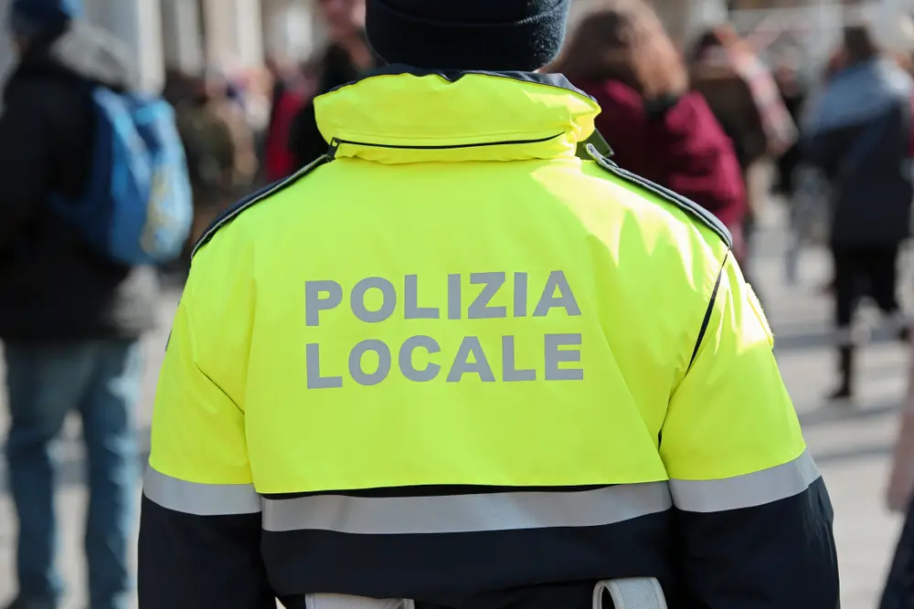Poliziotto italiano della Polizia Locale di spalle con giacca gialla alta visibilità in servizio urbano.