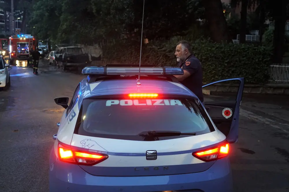 Poliziotto in servizio accanto a una volante della Polizia di Stato con luci accese e attrezzatura tecnica operativa.