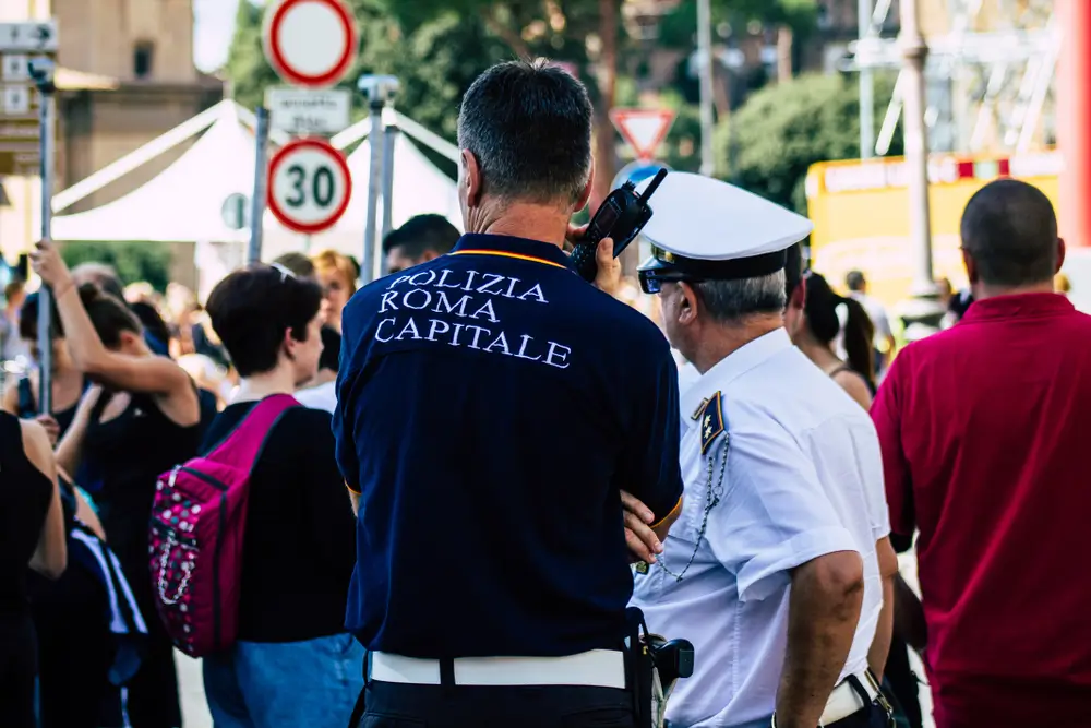 Un poliziotto in divisa comunica via radio mentre coordina le operazioni sul campo in un'area urbana affollata.