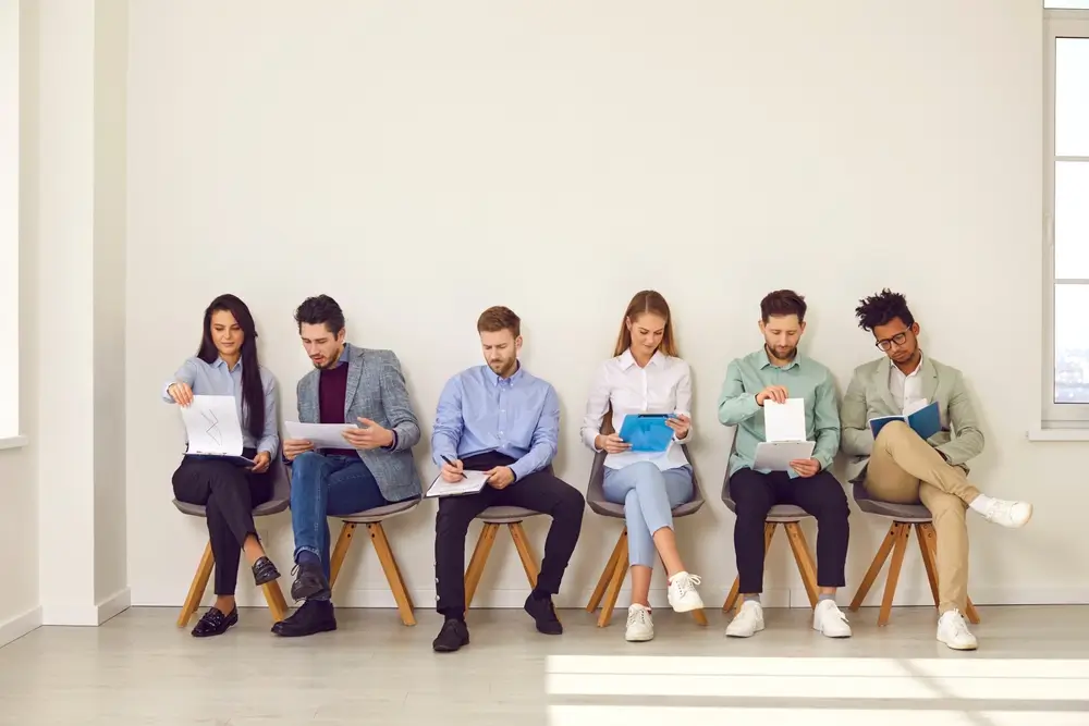 Candidati seduti in fila mentre consultano documenti e appunti in attesa di un concorso pubblico.