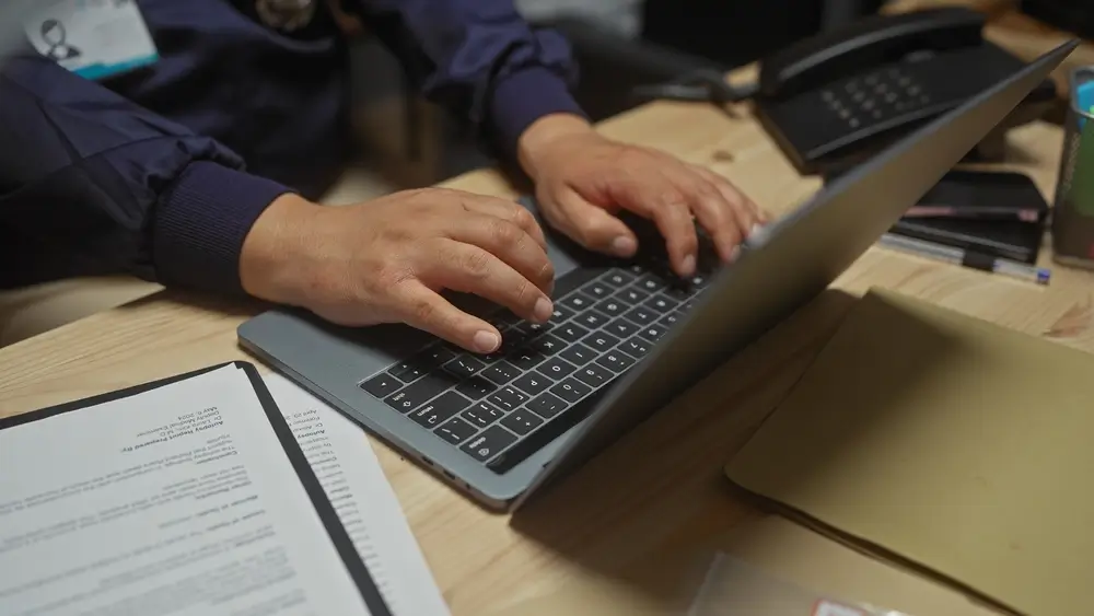 Poliziotto in ufficio lavora al computer sulla sua scrivania tra documenti e faldoni della Polizia di Stato.