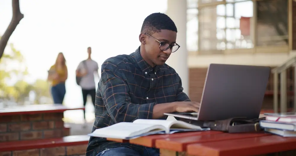 Candidato al concorso utilizza un laptop e libri per studiare e verificare i materiali del simulatore online.